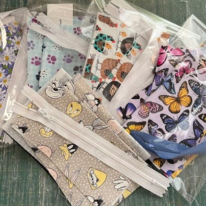 May include: A set of six fabric face masks in clear plastic bags. The masks feature various patterns, including butterflies, chickens, paw prints, and cartoon characters. The bags are sealed with a white zipper.