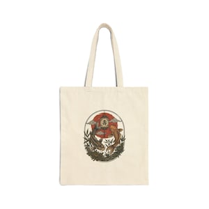 May include: A beige canvas tote bag featuring a centered oval graphic. The illustration depicts two koi fish swimming around a hanging lantern with Japanese text, set against a red sun, stylized clouds, and green bamboo foliage.
