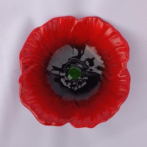 Pode incluir: Uma flor de papoula de vidro vermelho com um centro preto e verde. A flor é uma peça decorativa e tem um acabamento brilhante.