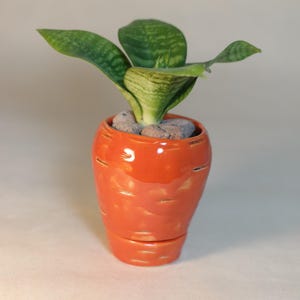 Puede incluir: Una planta serpiente verde en una maceta de cerámica naranja brillante con forma de zanahoria.