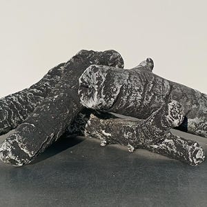 Op de afbeelding: Een set van drie zwarte en grijze kunststammen voor een open haard. De stammen zijn gemaakt van een realistisch uitziend materiaal en hebben een getextureerd oppervlak.