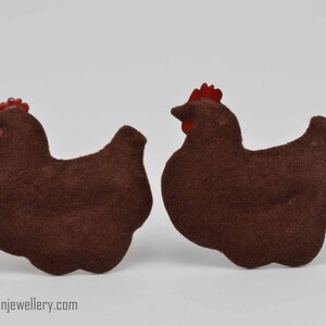 Puede incluir: Dos adornos de pollo de fieltro marrón con crestas de fieltro rojo. Los pollos están mirando en direcciones opuestas.