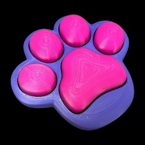May include: A purple paw-shaped silicone fidget toy with pink dimples. The toy is designed to be squeezed and pushed to relieve stress.