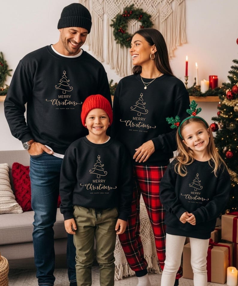 May include: A family wearing matching black sweatshirts with a gold Christmas tree design and the words "MERRY CHRISTMAS AND HAPPY NEW YEAR". The family is standing in front of a Christmas tree and decorations.