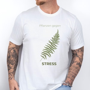 May include: White t-shirt with a green fern illustration and the word "STRESS" below it. The text "Pflanzen gegen" is above the fern. The shirt is made of a soft material.