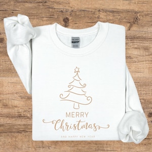 May include: A white crew neck sweatshirt with a gold Christmas tree design and the words "MERRY CHRISTMAS" and "AND HAPPY NEW YEAR" in gold script. The sweatshirt is made of a soft material.