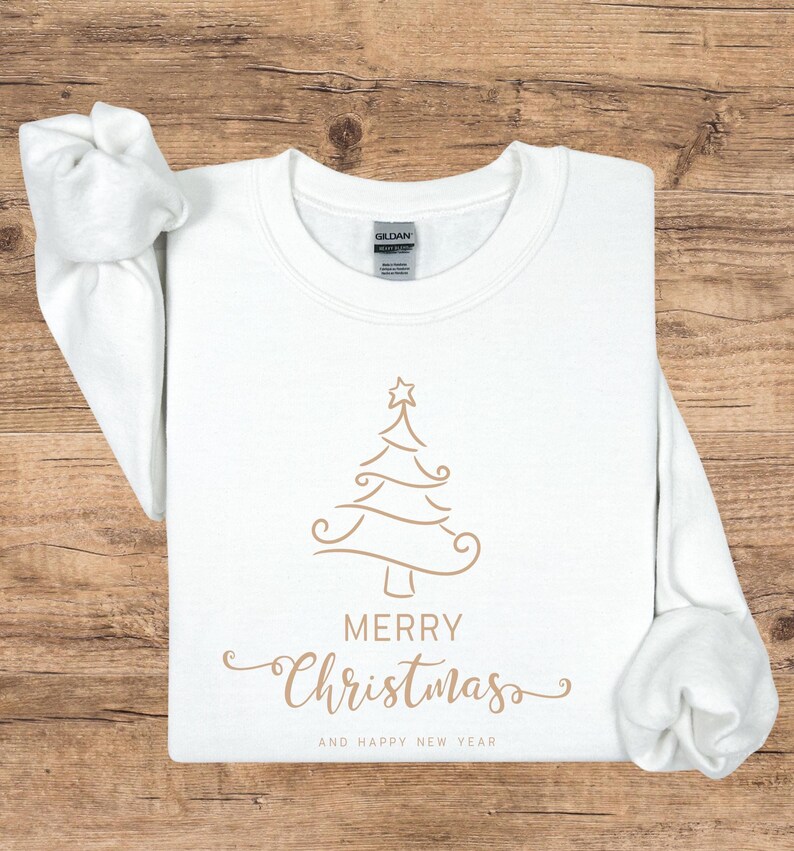 May include: A white crew neck sweatshirt with a gold Christmas tree design and the words "MERRY CHRISTMAS" and "AND HAPPY NEW YEAR" in gold script. The sweatshirt is made of a soft material.