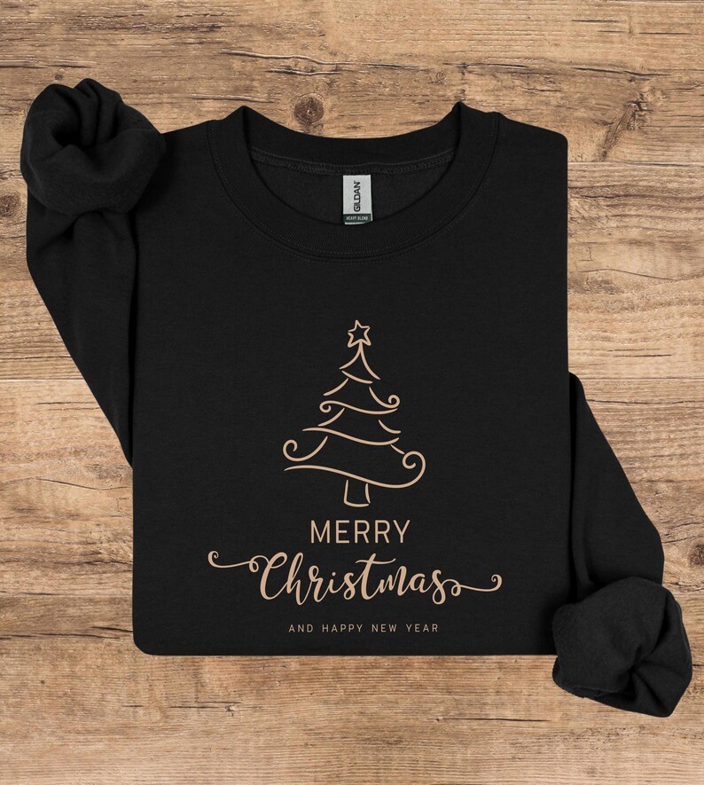 May include: Black sweatshirt with a gold Christmas tree design and the words "MERRY Christmas AND HAPPY NEW YEAR" in a decorative font. The sweatshirt is made of a soft material and is perfect for the holiday season.