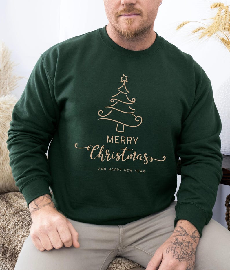 May include: Dark green sweatshirt with a gold-colored Christmas tree design and the words "MERRY CHRISTMAS AND HAPPY NEW YEAR". The sweatshirt is a crew neck style.