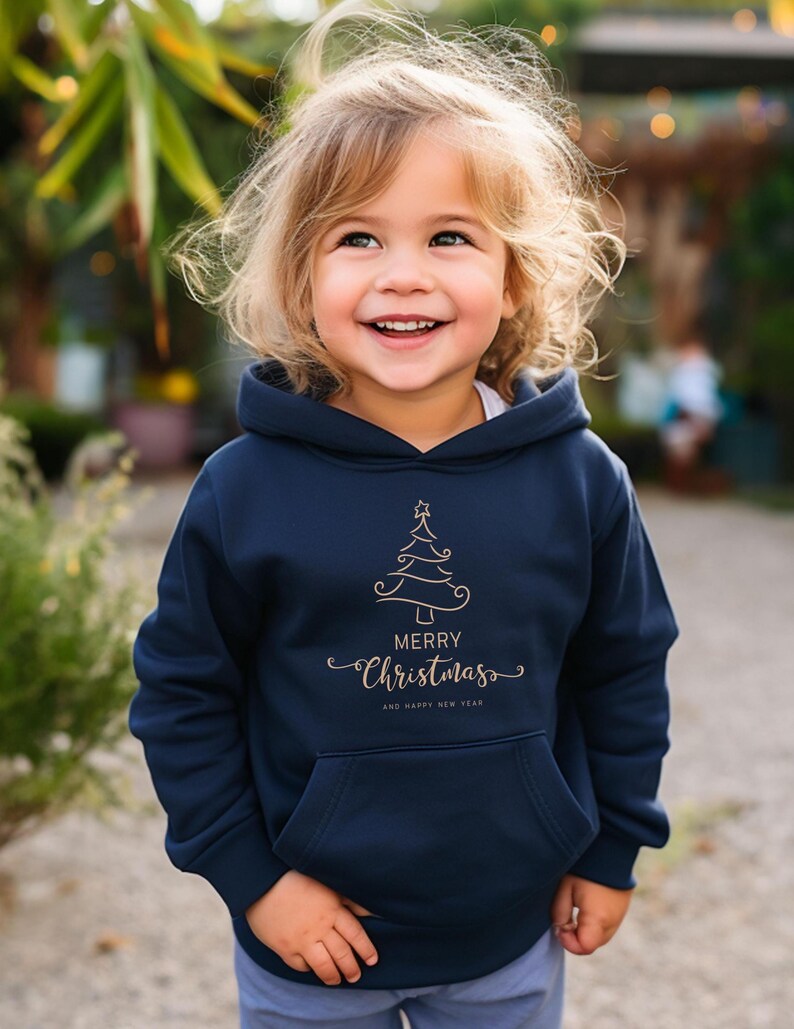May include: A navy blue hooded sweatshirt with a front pocket. The sweatshirt features a gold-colored Christmas tree design and the words "Merry Christmas" and "And Happy New Year" in a script font.