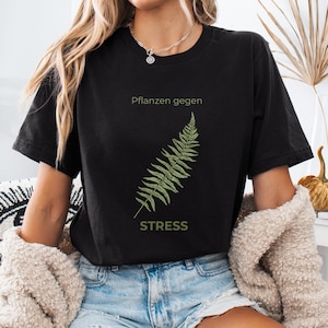 May include: Black t-shirt with a green fern illustration and the text "Pflanzen gegen STRESS". The shirt is made of a soft material and is suitable for casual wear. The design is simple and nature-inspired.