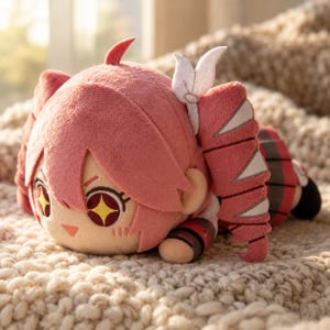 Può includere: Un peluche raffigurante un personaggio con capelli rosa acconciati in due code, decorati con accessori bianchi. Il personaggio ha grandi occhi a forma di stella gialli e rossi, un naso piccolo e indossa un completo rosso e nero con dettagli bianchi.