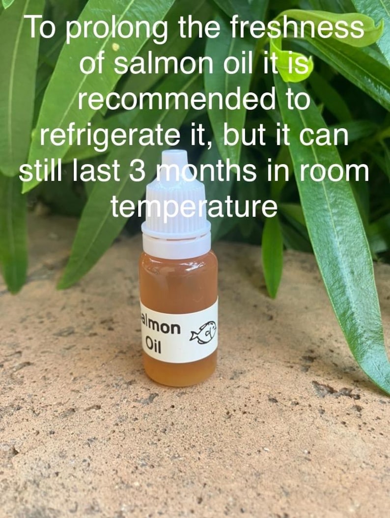 May include: A small, clear plastic dropper bottle filled with amber-colored salmon oil, featuring a white label with the text 'Salmon Oil' and a fish icon. The text on the image reads: 'To prolong the freshness of salmon oil it is recommended to refrigerate it, but it can still last 3 months in room temperature.'