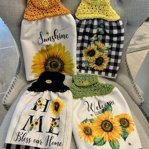 Könnte beinhalten: Vier dekorative Küchentücher mit Häkeloberteilen. Die Handtücher zeigen Sonnenblumenmotive und die Aufschriften "Sunshine", "Home Bless our Home" und "Welcome Sunshine". Die Handtücher haben schwarz-weiß karierte Muster.
