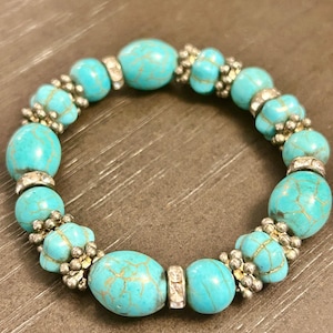 May include: Turquoise beaded bracelet with silver accents. The bracelet features oval and round turquoise beads with a gold-colored veining pattern. Silver-colored beads and rhinestone spacers add detail to the jewelry.