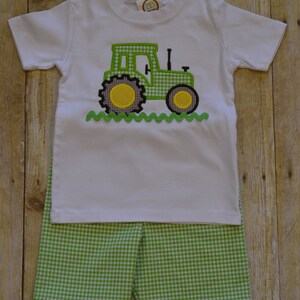 K&ouml;nnte beinhalten: Ein wei&szlig;es T-Shirt mit einem gestickten Traktor-Design in Gr&uuml;n und Schwarz. Das Shirt wird mit gr&uuml;n-wei&szlig; karierten Shorts kombiniert.