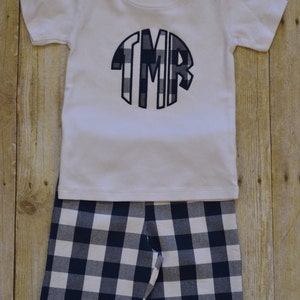K&ouml;nnte beinhalten: Ein wei&szlig;es T-Shirt mit kurzen &Auml;rmeln und einem marineblauen und wei&szlig;en karierten Monogramm auf der Vorderseite. Das Shirt wird mit marineblauen und wei&szlig;en karierten Shorts kombiniert.