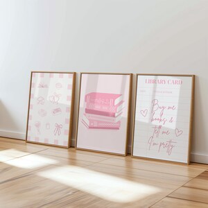 Pode incluir: Três impressões de arte emolduradas em tons de rosa claro e branco. As impressões apresentam ilustrações de livros, um cartão de biblioteca e outros elementos decorativos. O texto no cartão da biblioteca diz "Buy me books & tell me I'm pretty".