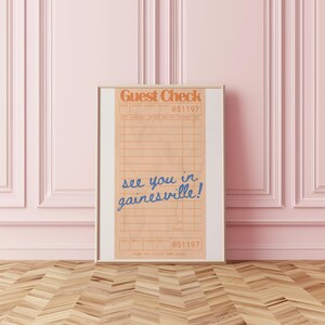 Peut inclure: Impression encadr&eacute;e d'un re&ccedil;u de restaurant de style vintage. Le haut indique "Guest Check" en orange, avec le num&eacute;ro "051197". En dessous, en &eacute;criture bleue, on lit "see you in gainesville!"