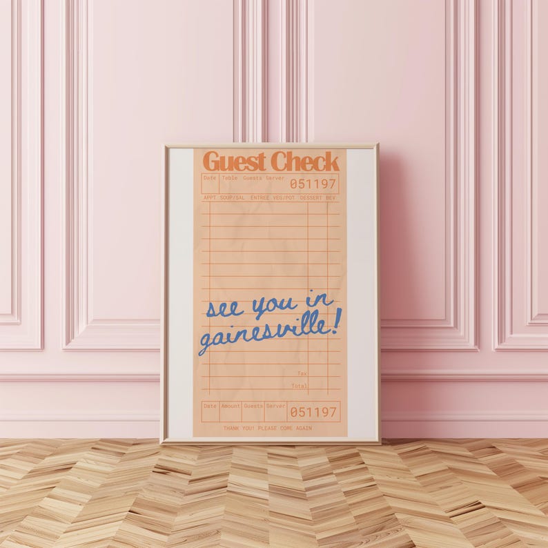 Peut inclure: Impression encadr&eacute;e d'un re&ccedil;u de restaurant de style vintage. Le haut indique "Guest Check" en orange, avec le num&eacute;ro "051197". En dessous, en &eacute;criture bleue, on lit "see you in gainesville!"