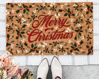 May include: A rectangular doormat with the words "Merry Christmas" in red script, surrounded by a pattern of green leaves and white berries. The doormat is on a gray and white checkered rug.