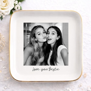May include: A white square ceramic tray with a gold rim, featuring a black and white photo of two young women. The phrase "Love you Bestie" is written in cursive below the photo. Decorative elements include a candle and flowers.