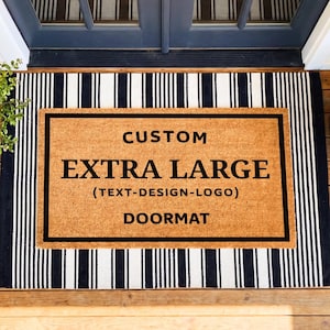 May include: An extra large custom doormat with a black and white striped border. The center of the doormat is a natural tan color with the words "CUSTOM EXTRA LARGE (TEXT-DESIGN-LOGO) DOORMAT" in black block letters.