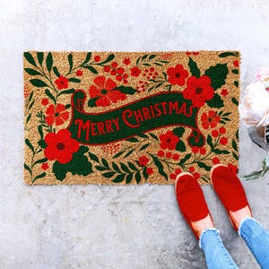 Christmas doormat with a centered Merry Christmas greeting framed by red flowers, berries and deep green foliage. The colorful botanical layout creates a festive holiday welcome mat for the front door and works naturally with red and green Christmas porch decor, seasonal entryway styling and floral holiday decorations.
