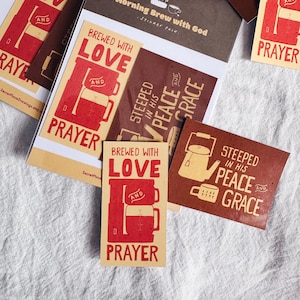 May include: A selection of brown and cream stickers with coffee-related designs. The stickers display phrases such as "Brewed with Love" and "Steeped in His Peace and Grace", alongside illustrations of coffee cups and teapots. The stickers are arranged on a white fabric surface.