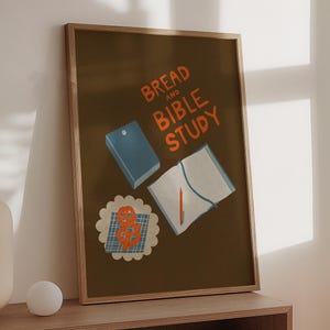 May include: A brown framed poster with the text "BREAD AND BIBLE STUDY" in orange lettering. The poster features illustrations of a blue notebook, a white notebook with a pen, and a plate of orange pretzels.