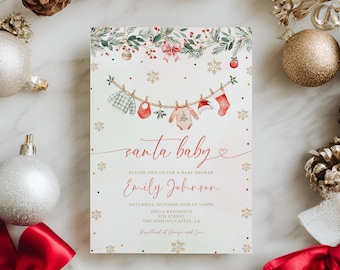 May include: A baby shower invitation with the text "santa baby" in red script. The invitation features a clothesline with baby clothes and snowflakes. The invitation is surrounded by Christmas ornaments and decorations.