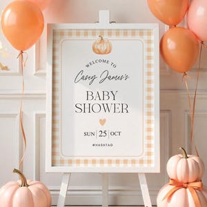 May include: A baby shower sign on a white easel, surrounded by orange and pink balloons and pumpkins. The sign reads "Welcome to Casey James's Baby Shower" with the date "Sun 25 Oct" and a hashtag. The pumpkins are in varying sizes and shades of pink.