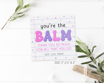 May include: A pink and purple card with the text "you're the BALM" in a playful font. The card also includes the text "Thank you so much for all that you do" and "With love, Jenny". The card is on a white background with a wooden surface and a green plant.