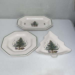 May include: Three white ceramic serving dishes featuring a Christmas tree design with gifts at the base. The set includes one octagonal platter, one octagonal plate, and one tree-shaped dish, all accented with a thin green rim and textured edges.