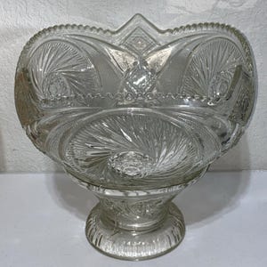 Puede incluir: Bol para servir de vidrio transparente con intrincados patrones grabados. El cuenco presenta una base de pedestal y un borde festoneado. El diseño incluye formas arremolinadas y geométricas, creando una estética vintage. Ideal para exhibir fruta o servir platos.