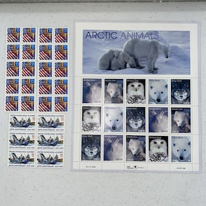 May include: A selection of vintage postage stamps. The stamps feature the American flag, a naval ship, and arctic animals. The arctic animal stamps depict polar bears, arctic foxes, snowy owls, and gray wolves. The stamps are in various sizes and colours.