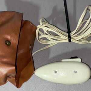 May include: A white electric fabric scissors with a brown leather case and a white cord with a plug. The scissors have a black button and the text "SCOT" on the side.