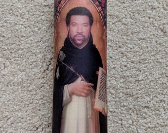 May include: A white candle with a colorful stained glass design featuring a portrait of a man with a beard and a book. The man is wearing a brown robe and holding a flower.