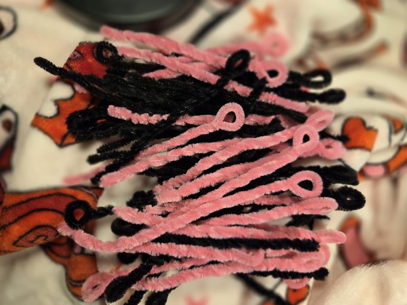 May include: A bunch of pink and black pipe cleaners. The pipe cleaners are twisted together and some are bent into loops.