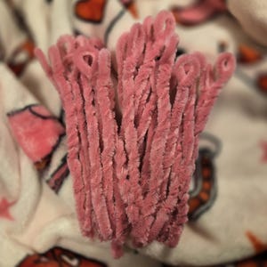 May include: A bunch of pink chenille stems, also known as pipe cleaners, are gathered together. The stems are soft and fuzzy.
