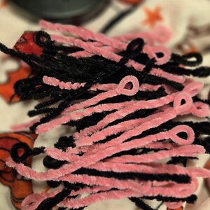 May include: A close-up of a bundle of pink and black pipe cleaners. The pipe cleaners are twisted together and have a fuzzy texture.