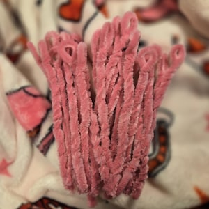 May include: A bunch of pink chenille stems, also known as pipe cleaners, are arranged together. The stems are soft and fuzzy, and they are perfect for crafting.