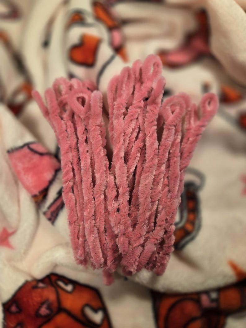 May include: A bunch of pink chenille stems, also known as pipe cleaners, are arranged together. The stems are soft and fuzzy, and they are perfect for crafting.