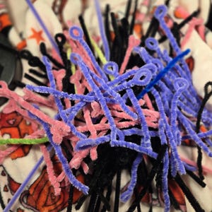 Puede incluir: Un mont&oacute;n de limpiapipas de colores en rosa, morado, negro y azul. Los limpiapipas est&aacute;n dispuestos en un patr&oacute;n aleatorio y est&aacute;n sobre una superficie con un patr&oacute;n blanco y rojo.