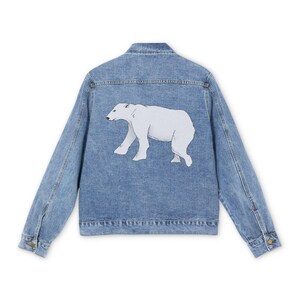 Puede incluir: Chaqueta vaquera azul claro con un diseño de oso polar blanco en la espalda. La chaqueta tiene un diseño clásico con cierre de botones, cuello y mangas largas. El oso polar está representado caminando.