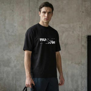 May include: A black t-shirt with the text "RUN WIN" and dark blue shorts. A gray duffel bag is being held, with the text "ATRACT" and "PERSEVERA ET VINCE" printed on it. The bag has black handles and a black side pocket. The person is wearing trainers.