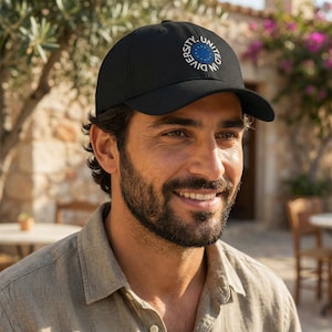 May include: Black baseball cap with a curved peak. The cap displays a circular emblem with the text "DIVERSITY. UNITED IN" and a blue and yellow design. The cap is worn by a person.