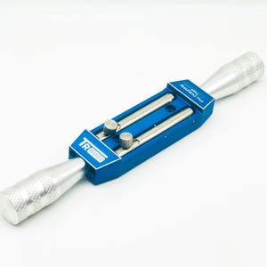 以下が含まれることがあります： 青と銀色のTR Maker Pro Polishing Tool。このツールは、2本の銀色のロッドと2つの銀色のノブが付いた青色のセンターセクションを備えています。端は銀色で、テクスチャード加工されたグリップが付いています。TR Makerのロゴが見えます。