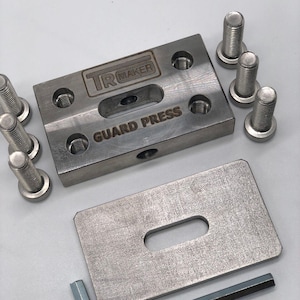 以下が含まれることがあります： 「TR MAKER」と「GUARD PRESS」の文字が刻まれた金属製のガードプレスセット。長方形のプレート、スロット付きの小さなプレート、いくつかのボルト、六角レンチが含まれています。コンポーネントは銀色です。