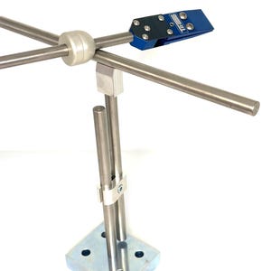 Pode incluir: Uma haste de metal prateada com uma braçadeira azul presa à extremidade. A haste está montada em uma base quadrada de metal prateado. A base tem quatro furos.